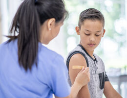 A healthcare provider puts an adhesive bandage on a boy's arm.